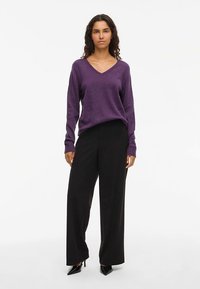 Μωβ πουλόβερ με v-λαιμόκοψη και μακριά μανίκια, συνδυασμένο με ψηλόμεσα μαύρα παντελόνια φαρδιάς γραμμής, με απαλή υφή και εφαρμοστή γραμμή.