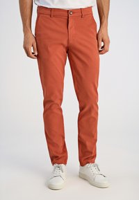 Rdzawoczerwone bawełniane spodnie o dopasowanym kroju, z przednim zamkiem błyskawicznym, zapięciem na guzik oraz bocznymi kieszeniami. W połączeniu z białymi trampkami.