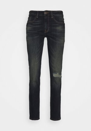 Mørkeblå denimjeans med en slim pasform, med let falming og et slidt område over knæet, afsluttet med traditionelle syningsdetaljer.