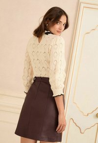 Pleteni kremasti pulover s dijamantnim uzorcima i otvorom na leđima, uparen s pripijenom mini suknjom od tamnosmeđe kože sa zatvaračem.