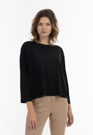Zwart langarmtop met een relaxte pasvorm en ronde hals, gemaakt van een gladde stof, gecombineerd met beige strakke broek.