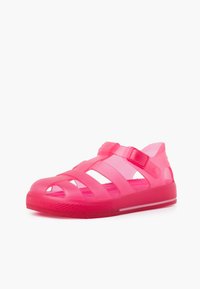 Pink transparent sandals featuring a crisscross strap design, a textured sole, and an adjustable strap for a secure fit.