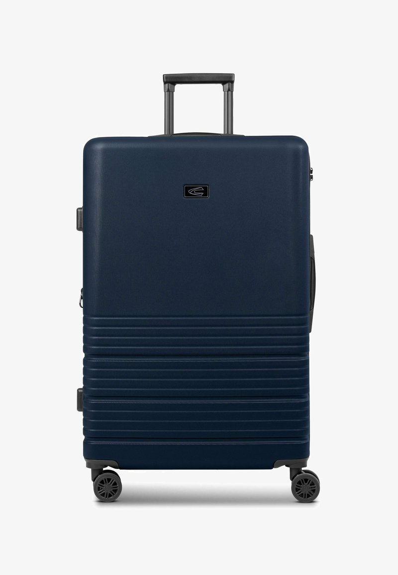 Valigia rigida blu navy con finitura testurizzata, scanalature verticali, manico retrattile e quattro ruote per la mobilità.