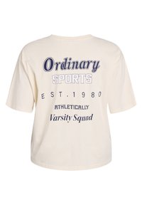 Cremefarvet kortærmet T-shirt med marineblå grafisk tekst: "Ordinary SPORTS EST. 1980 ATHLETICALLY Varsity Squad" på ryggen.