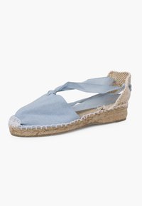 Šviesiai mėlynos kanvos espadrilės su kryžminėmis juostelėmis, jutinio pluošto viduriu ir balta siūle prie krašto. Atviras kulnas užtikrina kvėpavimą.