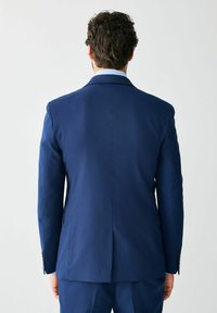 Tengerészkék, testre szabott zakó sima felülettel, hátul szellőzőnyílással és két gombos záródással. Finom varrásokkal és elegáns gallérral rendelkezik.