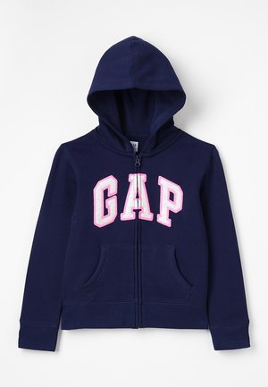 Sweat à capuche zippé bleu marine avec poches avant et capuche, avec de grandes lettres "GAP" roses et blanches sur la poitrine.