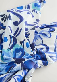 Kukallinen kangas, jossa on sinisiä ja turkooseja sävyjä valkoisella taustalla, sileä pinta ja pehmeä rosoinen ilme.