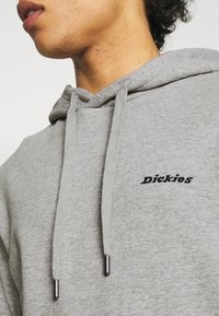 Felpa grigia realizzata in tessuto morbido con un design classico, dotata di cappuccio con coulisse e di un piccolo logo nero "Dickies" sul petto.