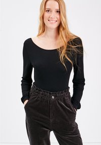 Body a maniche lunghe nera abbinata a pantaloni in velluto a coste marroni con vita elastica e tasche frontali. Texture liscia del body.