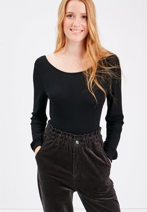 Body a maniche lunghe nera abbinata a pantaloni in velluto a coste marroni con vita elastica e tasche frontali. Texture liscia del body.