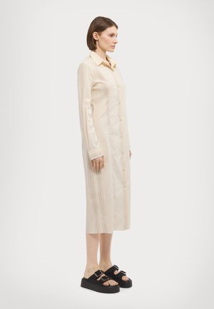 Lungo abito button-up beige chiaro con righe verticali, colletto sagomato e maniche lunghe. Indossato con sandali platform neri.