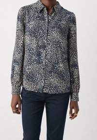 Camicia a bottoni blu navy in tessuto leggero, con un motivo a pois di colore crema e azzurro chiaro, maniche lunghe e colletto classico.