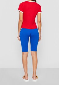 Camisa corta roja con mangas cortas y ribete blanco, combinada con pantalones capri azules ajustados. La tela parece suave; el diseño es entallado y casual.