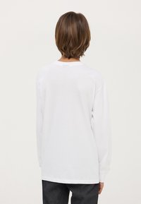 Maglietta bianca a maniche lunghe con scollo rotondo, realizzata in morbido cotone, con una vestibilità rilassata e orli cuciti; vista da dietro.