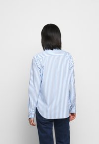 Blå och vit randig skjorta med knappar, långa ärmar och rundad nederkant. Synliga manschetter och en ryggsöm. Slät bomullstyg.