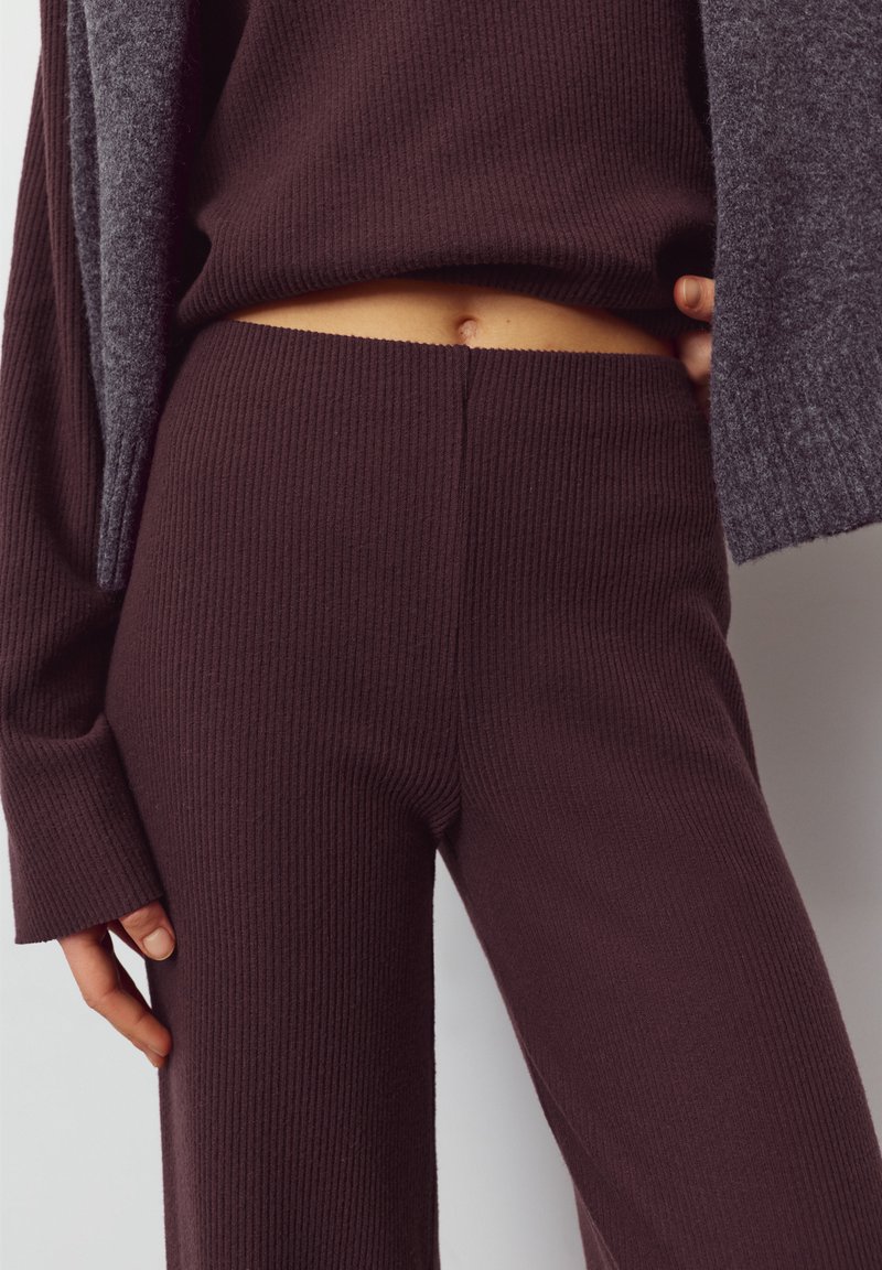 Temno rjav komplet iz rebrastega pletenega blaga z zgornjim delom in hlačami. Tkanina je teksturirana, z gostim in mehkim videzom. Komplet vključuje skrajšan zgornji del in hlače z širokimi hlačnicami.