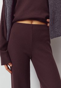 Donkerbruin geribd gebreid top- en broekset. Getextureerde stof met een dikke, zachte uitstraling. Heeft een cropped top en een ontwerp met wijde broekspijpen.