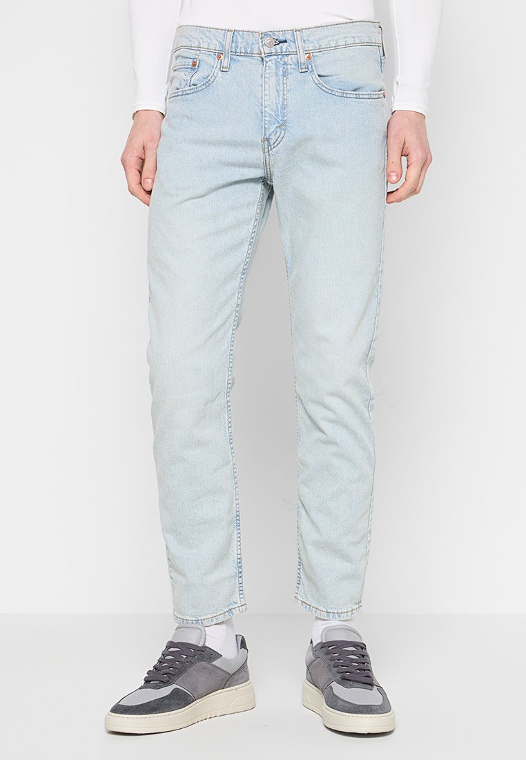 Jasnoniebieskie dżinsy w slim fit, z pięcioma kieszeniami i subtelnym przetarciem. W zestawieniu z szaro-białymi sneakersami.