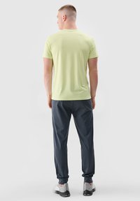 Lichtgroen T-shirt met korte mouwen, gecombineerd met donkergrijze, taps toelopende sweatpants en grijze sportschoenen, gezien vanuit de achterkant.