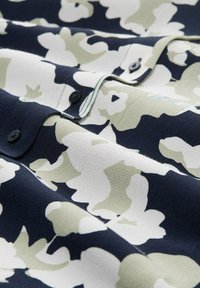 Tissu à motifs floraux en marine, blanc et olive. Texture lisse avec des boutons noirs et des accents rayés subtils près du col.