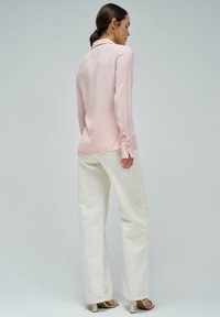 Camisa de manga larga rosa claro con cuello, con puños abotonados, combinada con pantalones anchos blancos y sandalias de tacón.