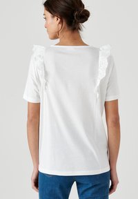 T-shirt bianco a maniche corte con ruffles in pizzo decorativi sulle spalle, tessuto morbido e vestibilità rilassata. Scollatura rotonda base.