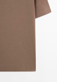 T-shirt marrone a maniche corte realizzato in morbido cotone; presenta un design semplice con orlo dritto e cuciture pulite.