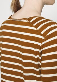 Brown and white striped long-sleeve shirt with a crew neck, featuring contrasting stitching along the shoulder seam and soft texture.