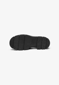 Black rubber shoe sole with horizontal grooves, rounded toe, and slight thickness. Textured surface for grip and durability.