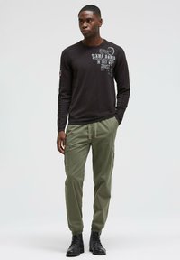 Schwarz langärmliges Shirt mit Grafiken, kombiniert mit olivgrünen Cargo-Hosen mit Seitentaschen, ergänzt durch schwarze Schnürstiefel.