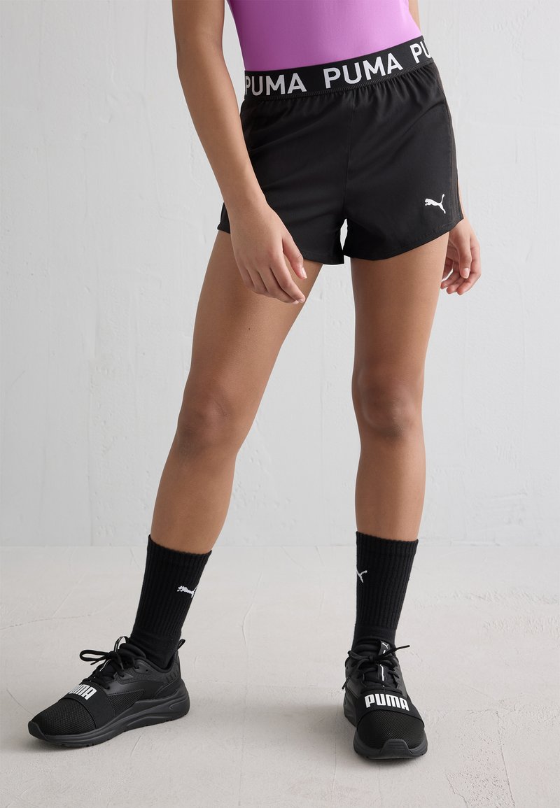 Mustat spordilühikesed püksid elastse vööga, millel on "PUMA" logo, koos mustade sokkide ja tennisetossudega. Sile kangas ja lihtne disain.