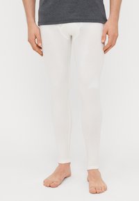 Λευκά κολάν φτιαγμένα από ένα απαλό, ελαστικό υλικό. Κομψός σχεδιασμός με μαλακή μέση και χωρίς ραφές, φορεμένα με γυμνά πόδια.