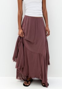Long, flowy skirt in a muted mauve color, featuring layered ruffles and a raw hem. Made from lightweight fabric, with an elastic waistband.