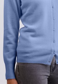 Ljusblå cardigan, tillverkad av mjukt stickat material. Har ribbade ärmslut och fåll, stickade knappar och en figurnära design.