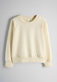 Krémová mikina s výstrihom okrúhleho tvaru, dlhými raglánovými rukávmi a rebrovanými manžetami a lemom, zobrazená na jednoduchom svetlom pozadí.