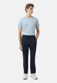 Jasnoniebieska koszulka z krótkim rękawem, granatowe spodnie zwężane z kieszeniami na zamek, elastyczna talia oraz białe buty sportowe. Gładkie tekstury na całej powierzchni.