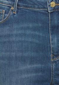 Chude niebieskie dżinsy o gładkiej fakturze, z złotymi dodatkami i kontrastowymi szwami, podkreślające klasyczny design pięciu kieszeni.