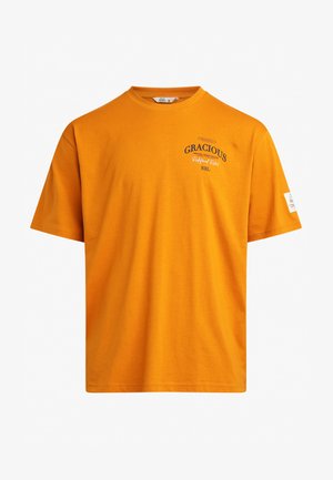Orange bomull t-shirt med kort ärm, rund hals och tryckt text. Har en etikett på vänster ärm och en rak nederkant.