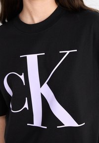 Czarna bawełniana koszulka z dużym jasnofioletowym logo "CK". Okrągły dekolt, krótkie rękawy i gładka faktura.
