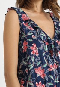 Blommönstrad klänning med marinblå bas, med volangpåsar vid axlarna och V-ringning, tillverkad av lättviktsmaterial.