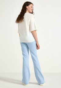 Cremiger Pullover mit kurzen Ärmeln, kombiniert mit hellblauen Schlaghosen. Einfaches Design, weiche Textur und minimalistischer Stil.