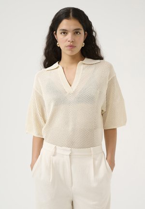 Maglietta a maniche corte in crema con scollatura a V e design con colletto, caratterizzata da un motivo diamante e tessuto testurizzato. Pantaloni su misura in abbinamento.