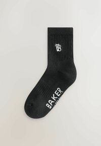 Sort bomuldsstrømpe med ribbet kant. Har et hvidt logo "TB" nær toppen og "BAKER" trykt på siden i hvid. Designet til afslappet brug.