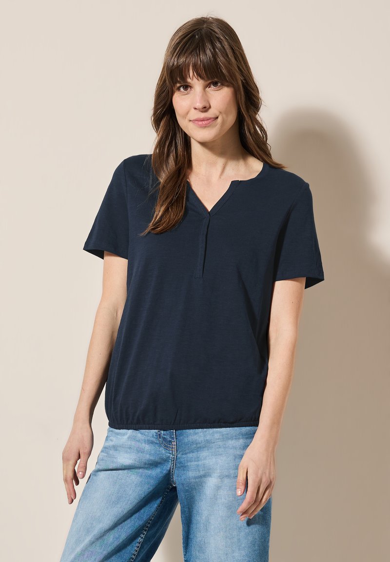 Mörkblå t-shirt med kort ärm och V-ringning, avslappnad passform och elastisk nederkant; slät tyg med en lätt lyster. Bärs med ljusblå jeans.