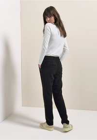 Černé teplákové kalhoty s elastickým pasem, bočními kapsami a kónickým střihem nohavic. Kombinovány s bílým dlouhým tričkem a světlými teniskami.