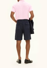 Pantaloni cargo navy con due tasche posteriori, realizzati in tessuto leggero. Indossati con una maglietta polo rosa e scarpe nere.
