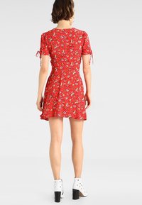Rotes Blumenkleid mit kurzen Ärmeln und Bindedetails, ausgestelltem Saum, aus leichtem Stoff. Getragen mit weißen Knöchelstiefeln.