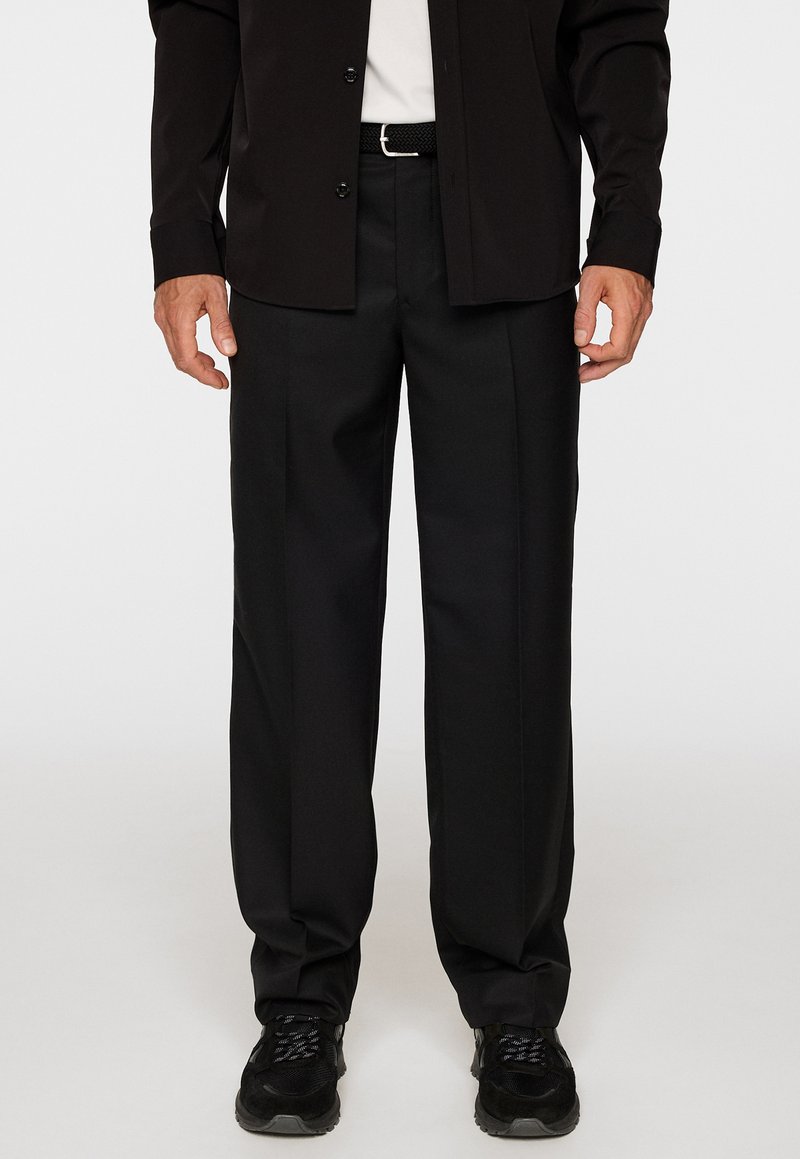 Svarta formella byxor i ett slätt tyg, med avspänd passform, framsydda veck och ett matchande svart bälte med silverdetaljer.
