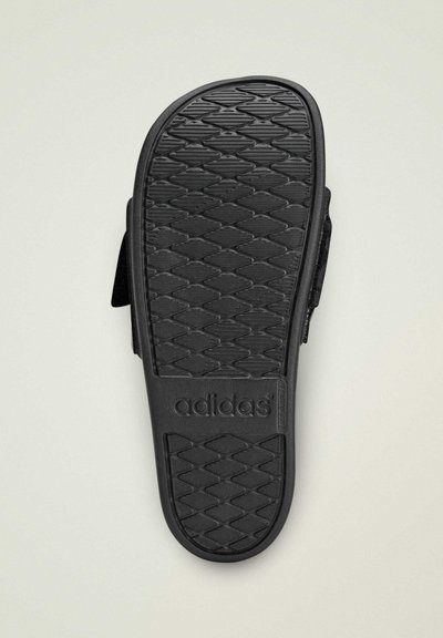 Semelle de sandale Adidas noire avec un motif antidérapant texturé, un logo, et une forme profilée pour le confort. Le matériau est un caoutchouc durable.